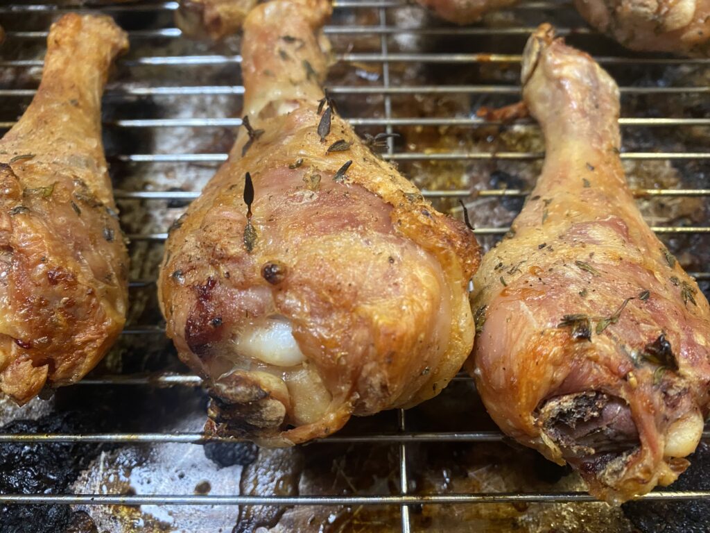 A closeup of crispy, herby chicken legs on a wire baking rack.
